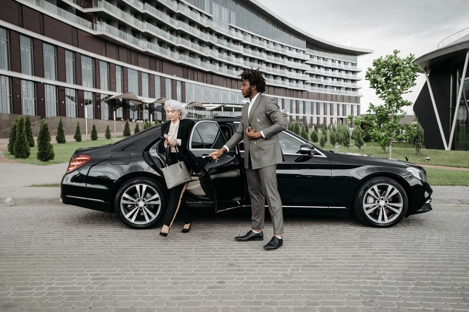 Chauffeur en costume aidant une cliente à descendre d'une berline