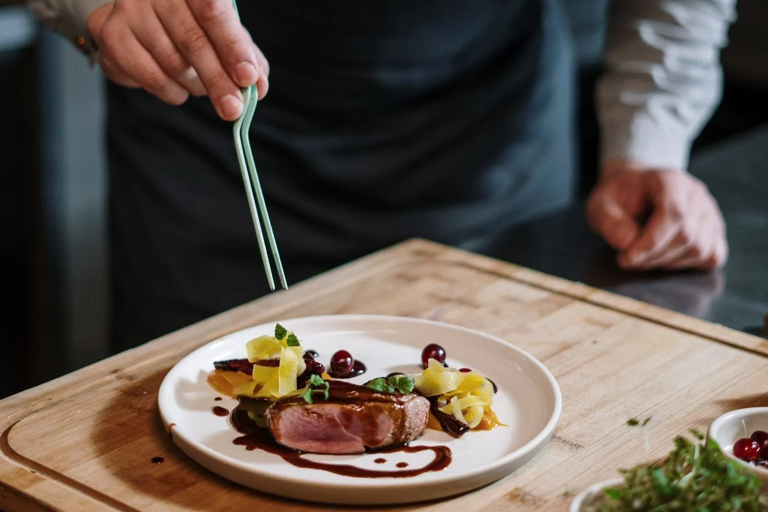 Chef en tablier dressant une assiette gastronomique à la pince